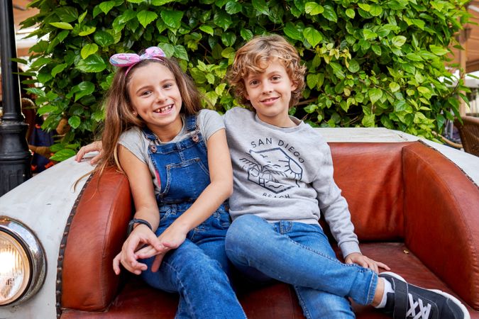 Cheerful boy and girl sitting on leather sofa in garden