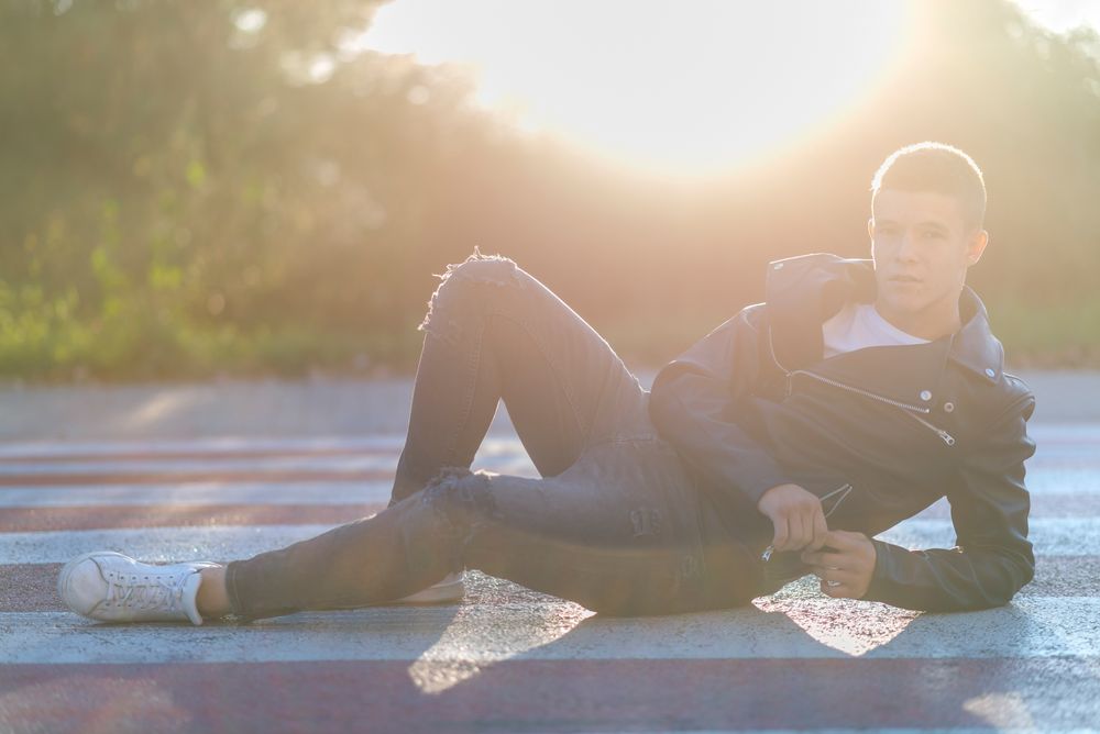 Teenage male wearing a leather jacket leaning back on concrete