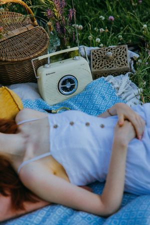 Woman laying on textile on green grass beside vintage radio