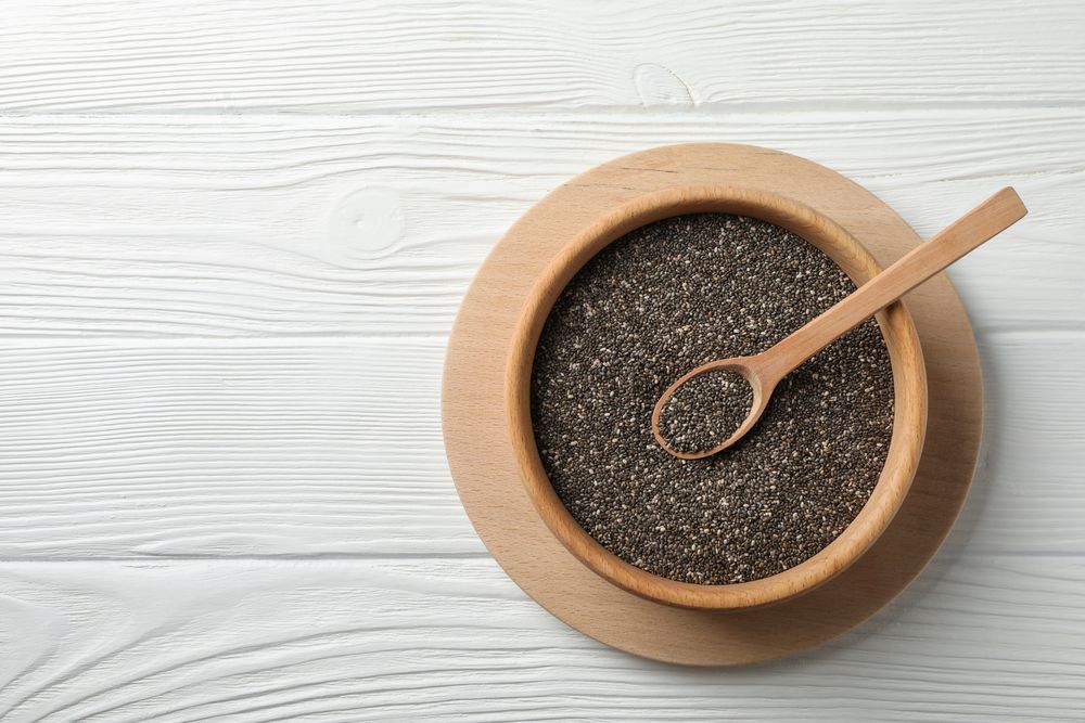 Wooden bowl with chia and spoon on wooden background, top view