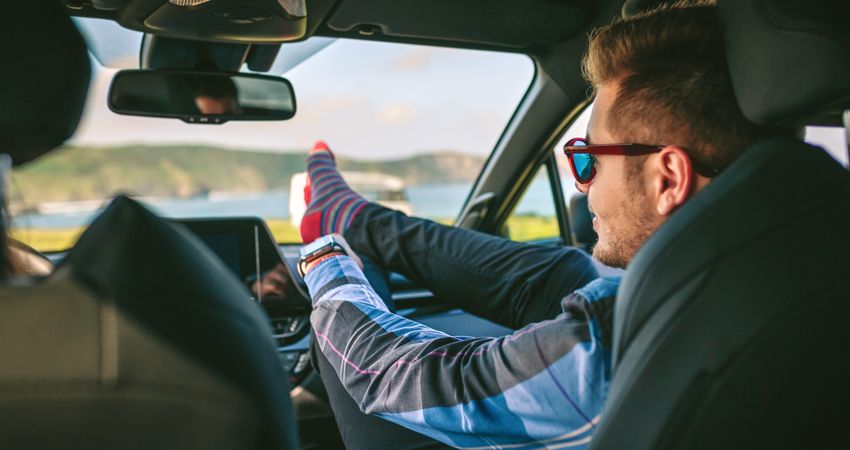 Young man resting feet up sitting on the car