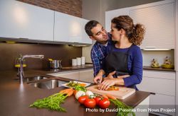 Loving couple in kitchen together as woman chops vegetables in kitchen with space for text 48pPq4