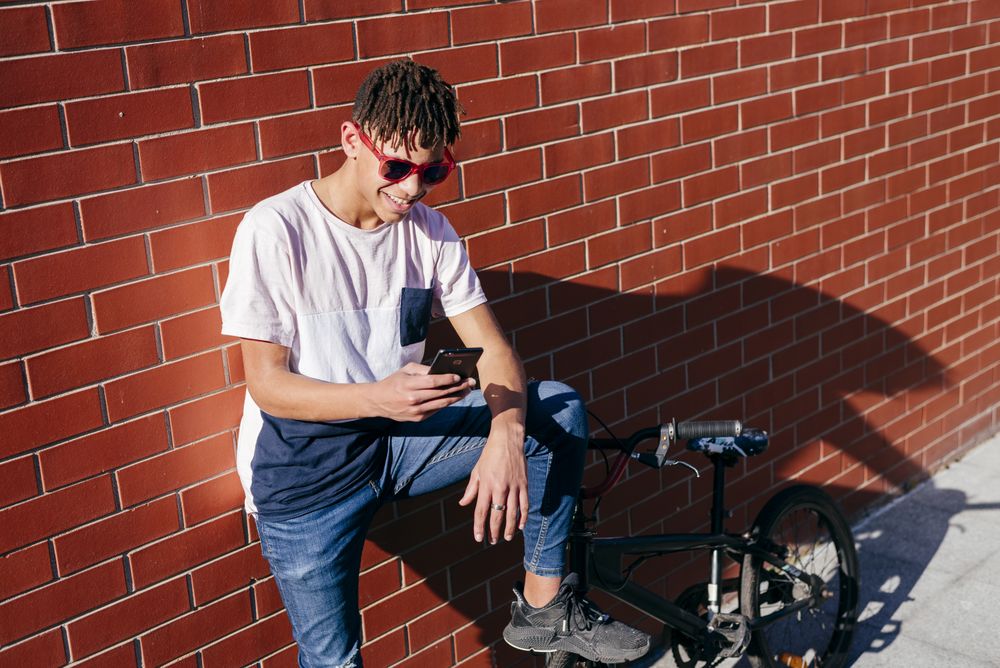 Young happy Black male browsing smartphone on bike