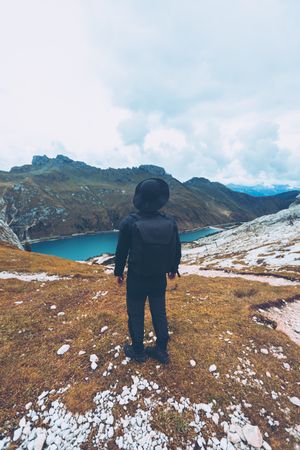 Back view of a man in dark outfit standing near lake in Italy