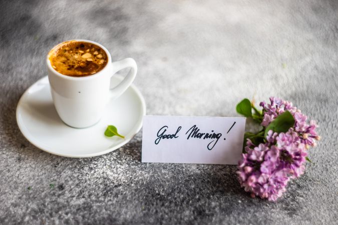 Cup of espresso and lilacs on grey counter with Good Morning note