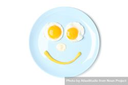 Looking down at blue plate with smiley face on it made of eggs and condiments 5zyBA0