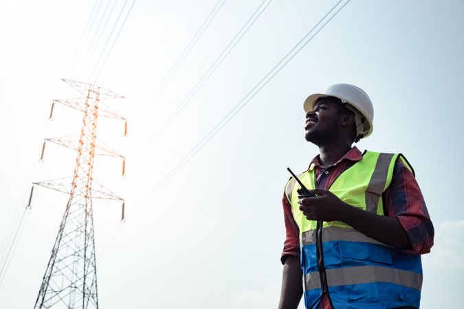 Low angle view of man with bump cap and green vest holding a talkie walkie