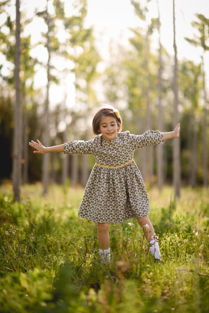Happy child standing in dress in field surrounded by trees, vertical