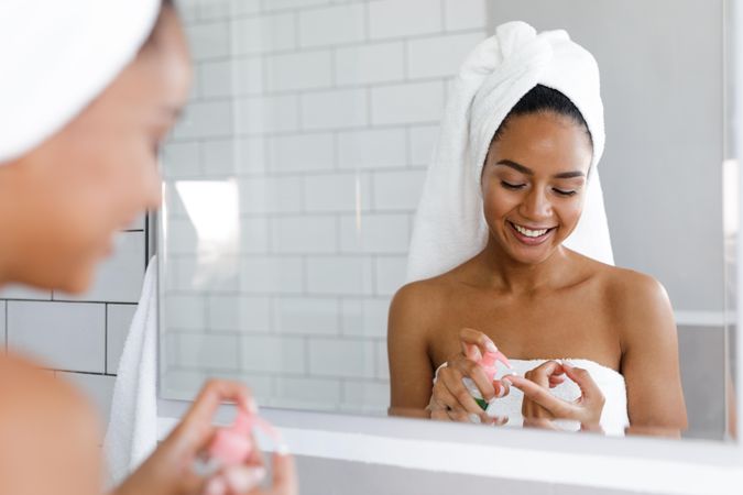 Black woman in towel squirting soap or cream onto her hand