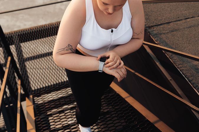 Blond woman with tattoos checking smart watch walking up staircase