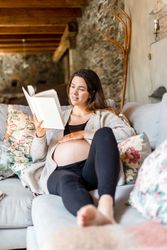 Relaxed pregnant woman enjoying reading a book on her home sofa