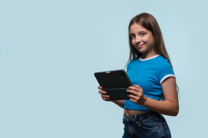 Girl holding tablet, looking engaged and happy with device.
