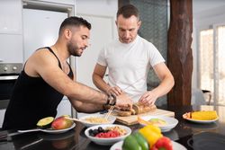 Male couple preparing vegetables and cutting bread for sandwich