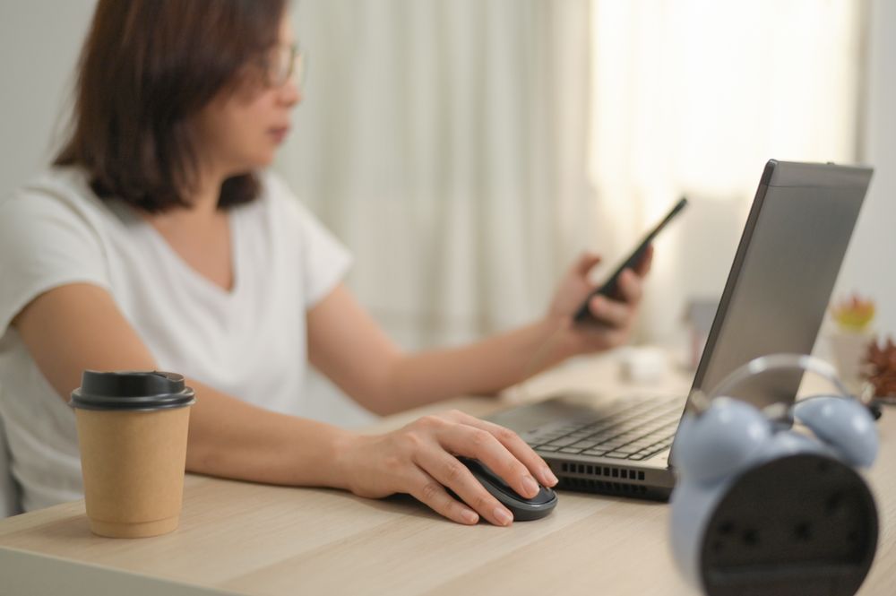 A woman hand holding on a mouse using a laptop working from home.