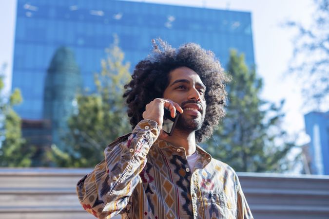 Handsome smiling man with curly hair using a mobile phone while standing outdoors
