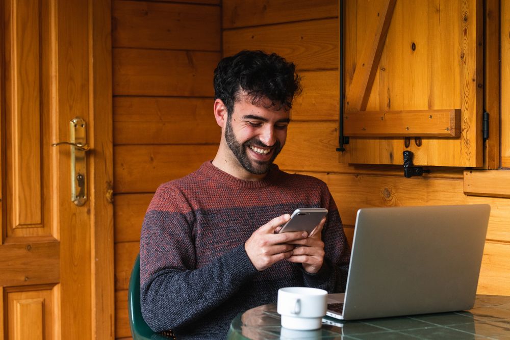 Cheerful man browsing on smartphone and working on terrace