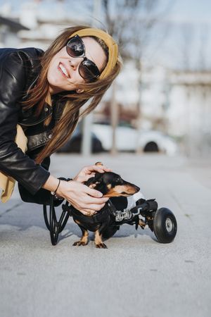 Smiling woman near dog with wheelchair on street