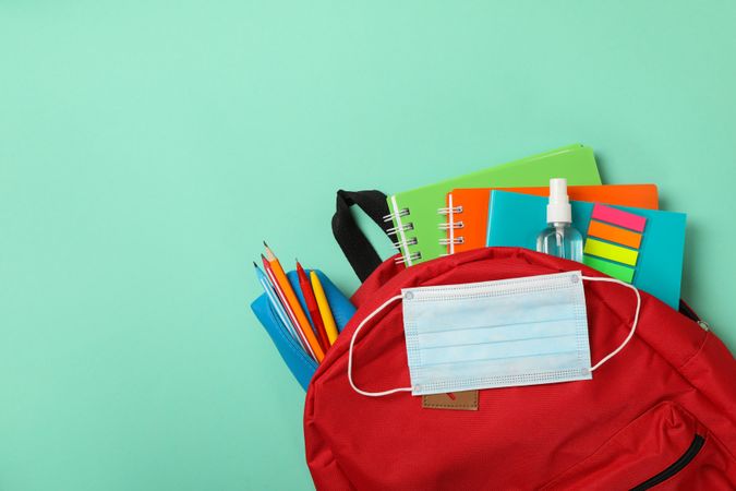 School supplies with medical mask and sanitizer on mint background
