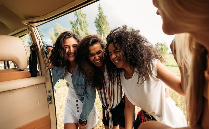 Group of friends on road trip laughing at van door
