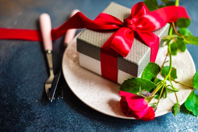 Table setting with red rose and bow wrapped gift