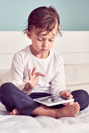 Serious boy playing game on tablet in bedroom