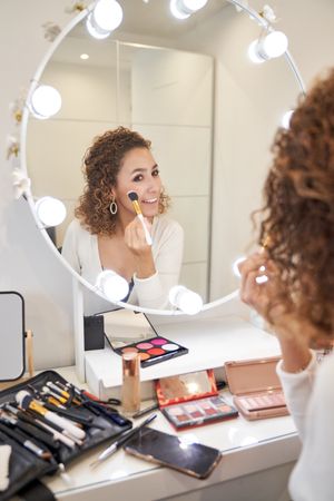 Smiling young female applying makeup on cheeks with brush
