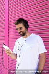 Man in headphones checking phone in front of pink wall 0Lzwr4