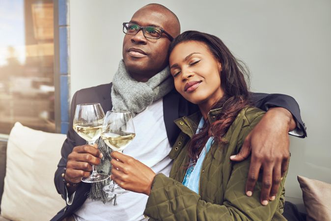 Black couple in each others arms in an outdoor restaurant with wine in hand
