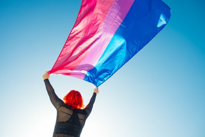 Back view of woman waving colorful flag under blue sky