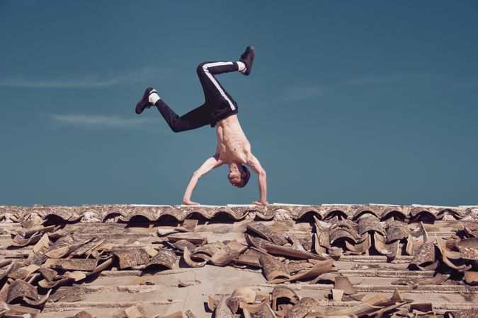 Flexible man performing tow handstand element of breakdance on rooftop