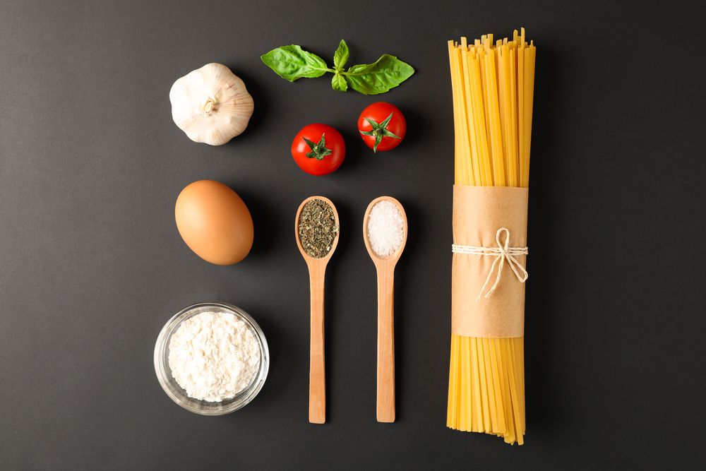 Flat lay composition with pasta ingredients on dark background, space for text