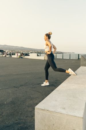 Athletic woman performing a lunge exercise in a public urban park by the sea