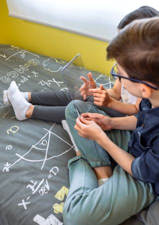 Unrecognizable children having fun with futuristic transparent tablet sitting over bed.