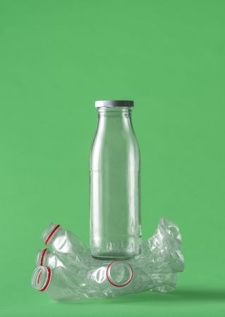 Glass over plastic bottles concept on a green background