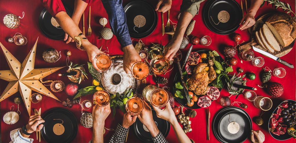 Group of people toasting with drinks at festive red table with cake, roast chicken, and decorations