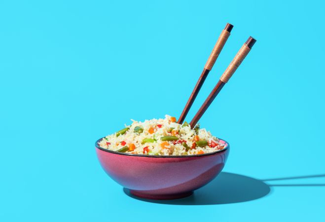 Bowl with fried rice and vegetables minimalist on a blue background