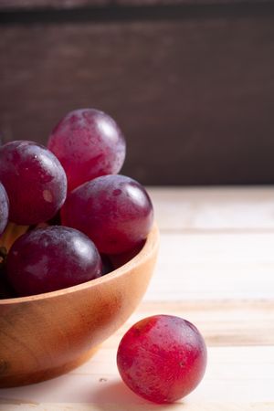 A bowl of red grapes sits on a wooden table