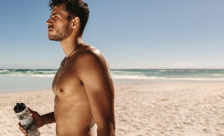 Shirtless man holding water bottle at a beach
