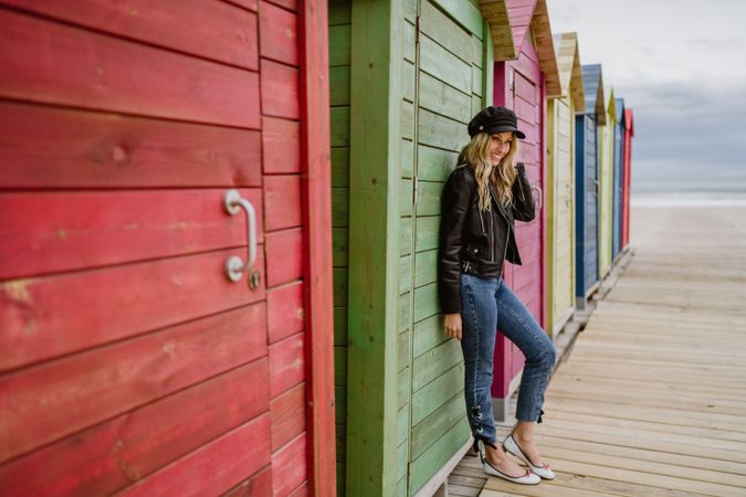 Stylish woman smiling and leaning on bright wooden cabins on beach