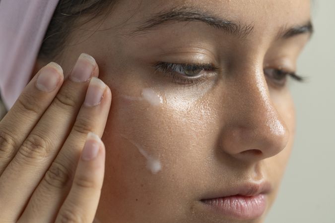 Macro shot of a woman massaging a hydrating serum or cream into the skin under her eyes