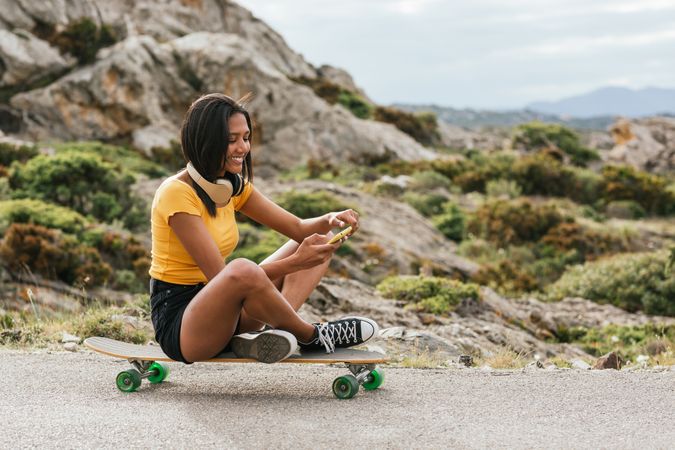 Cheerful woman using mobile phone while sitting on longboard