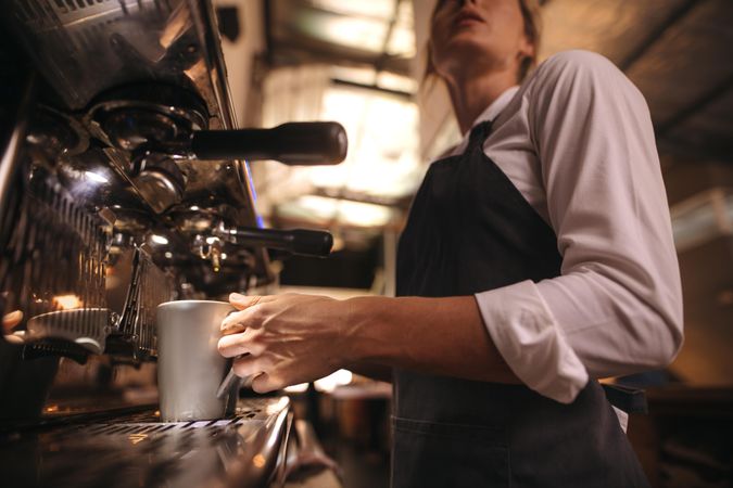 Woman working in cafe wearing apron making a coffee in machine