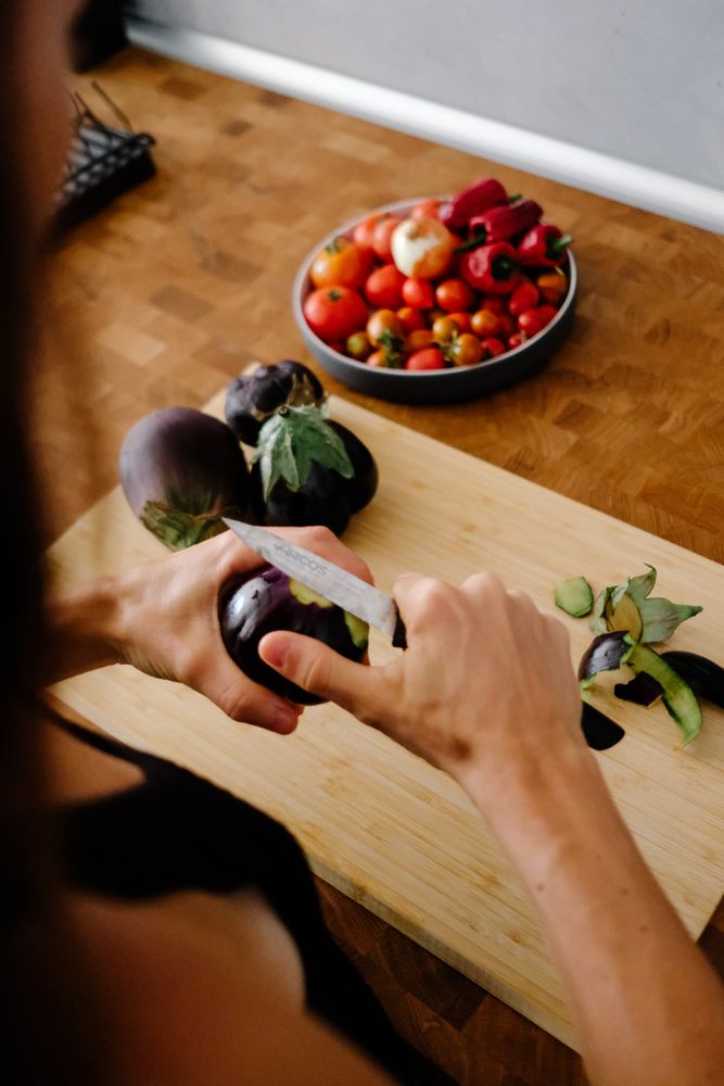 Person trimming fresh egg plants on wooden board