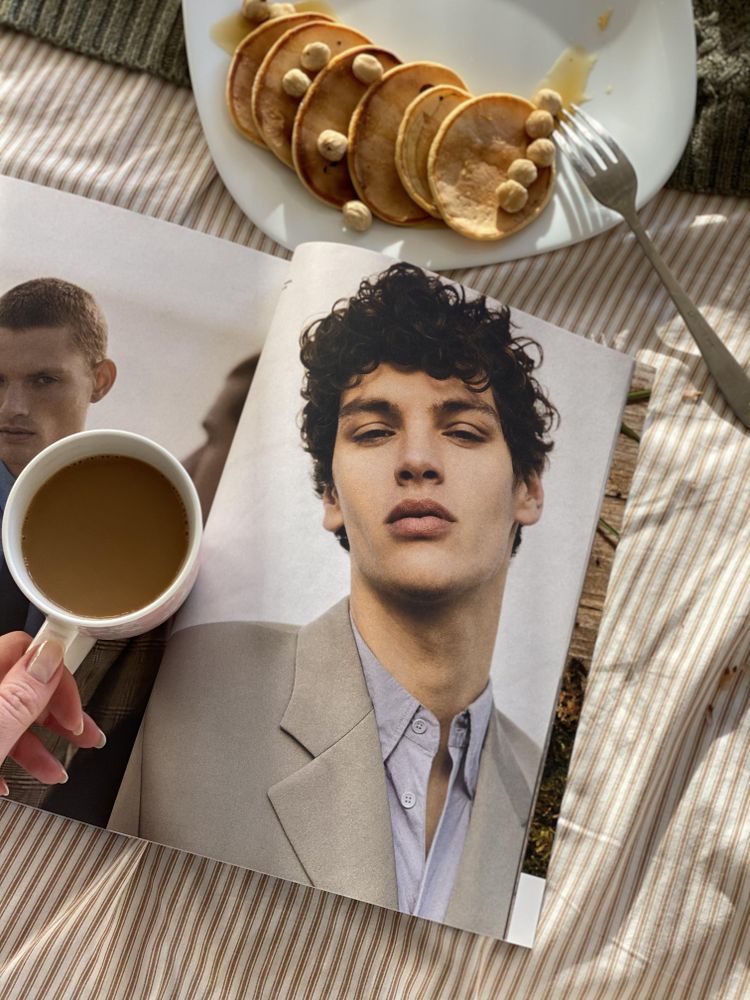 Person drinking coffee reading magazine with pancakes in bed