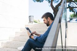 Man sitting on stairs outside checking digital tablet 5l1zV4