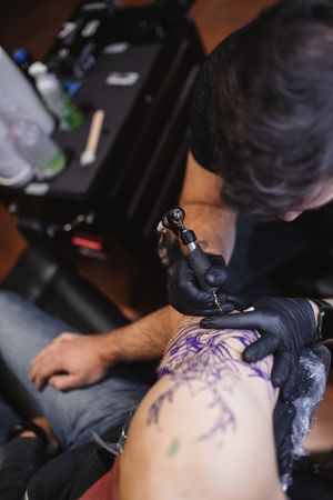 Master doing tattoo on forearm of male customer