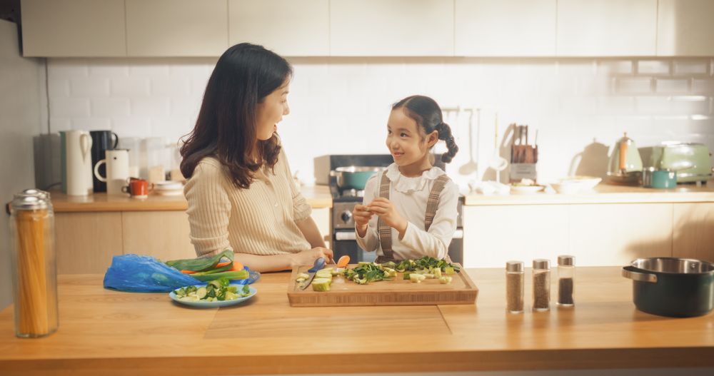 In the Kitchen: Korean Mother and Cute Little Daughter Cooking Together Healthy Dinner.