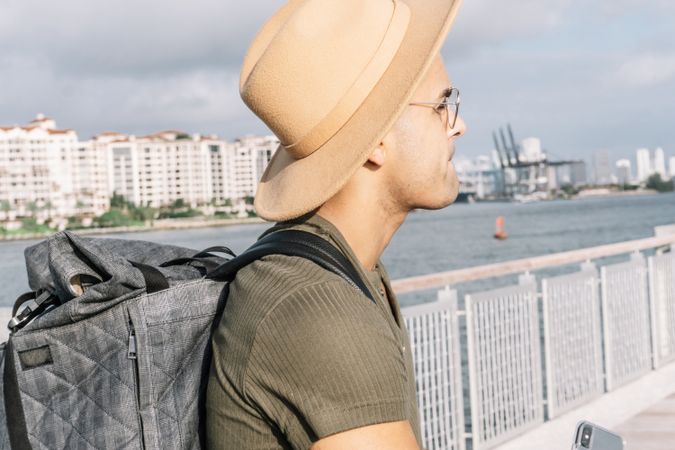 Side view of a man with a nice hat and glasses looking straight ahead carrying a backpack.