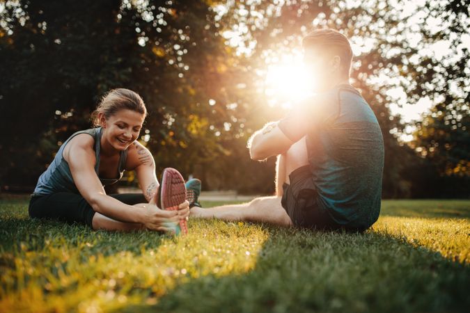 Fit young man and woman stretching in morning on grass