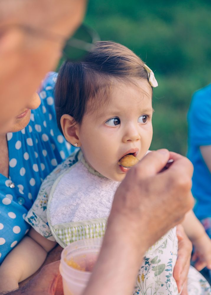 Man feeding baby girl sitting on a bench